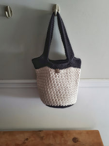Sand and black bag hanging on wall over wood bench. Bag has black base and handles.